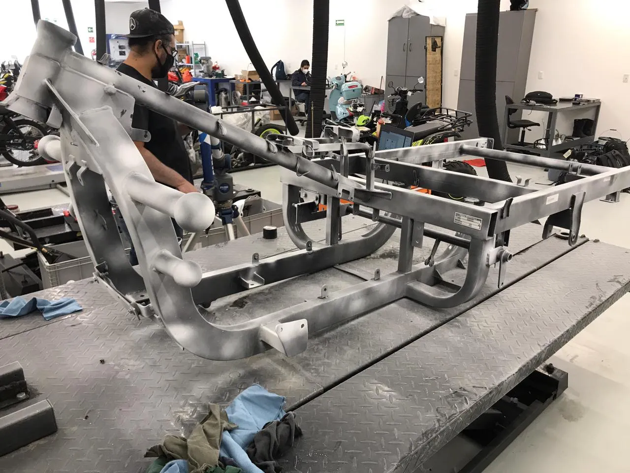 AxonID technician capturing the motorcycle frame with the FARO Scan Arm — point cloud visible on the screen in the background. Metrology workshop, technical lighting.